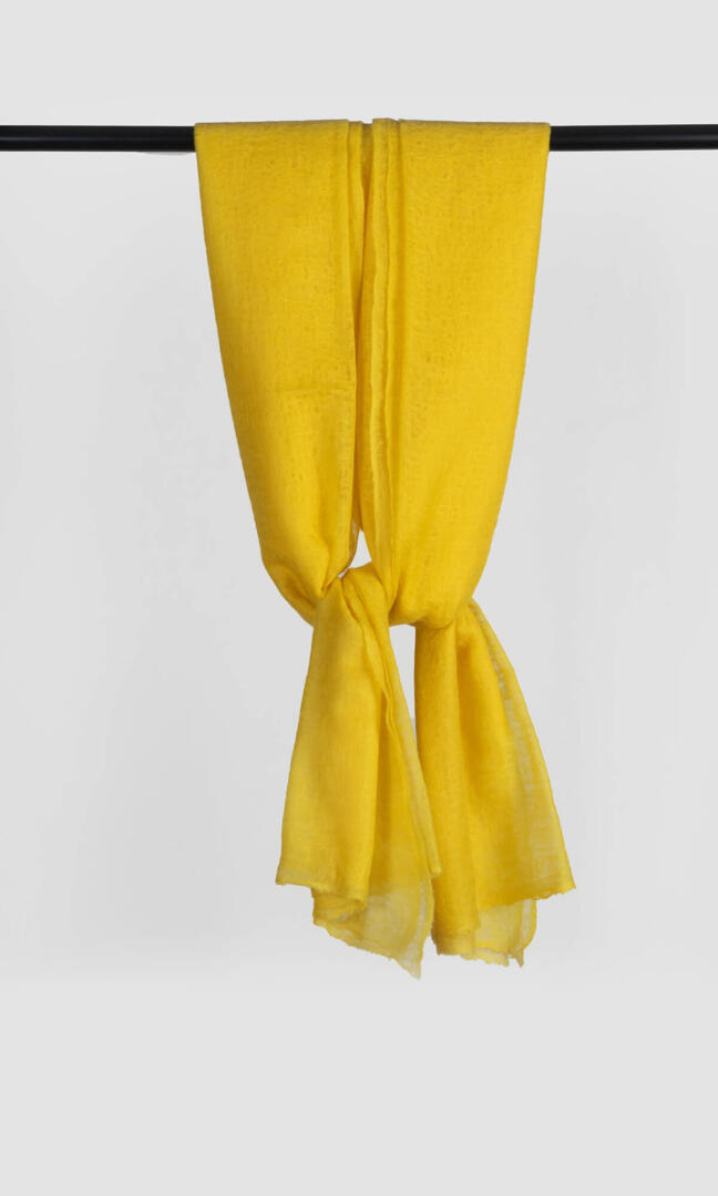 A nice photograph of handwoven 100% Pure Emperor Yellow Cashmere Shawl hanging from a bar to display the lightness and flow it carries.