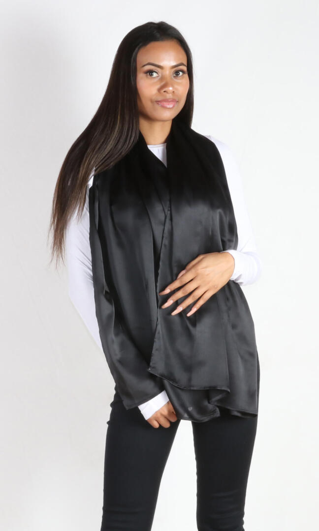 A 6 ft tall female model gracefully displays Aviator silk scarf in black spread in the front - 100% Plant Based Scarf Made From Rose Plant Yarn.