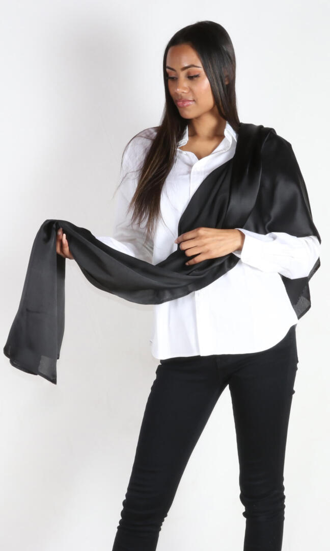 A 6 ft tall female model gracefully holds Aviator silk scarf in black - 100% Plant Based Scarf Made From Rose Plant Yarn.