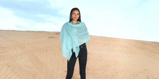 A person elegantly draped in a lightweight and versatile cashmere shawl, perfectly suited for desert climates, symbolizing comfort and protection against changing weather conditions.