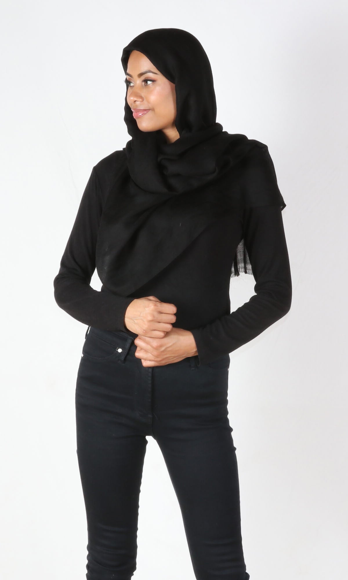 A beautiful 5ft 8 inches tall female model in a profile pose displays a 100% pure handmade black cashmere shawl wrapped around her head and draped nicely around her neck to convey the message of how the cashmere shawl can be used in a different environments when circumstances call for it.