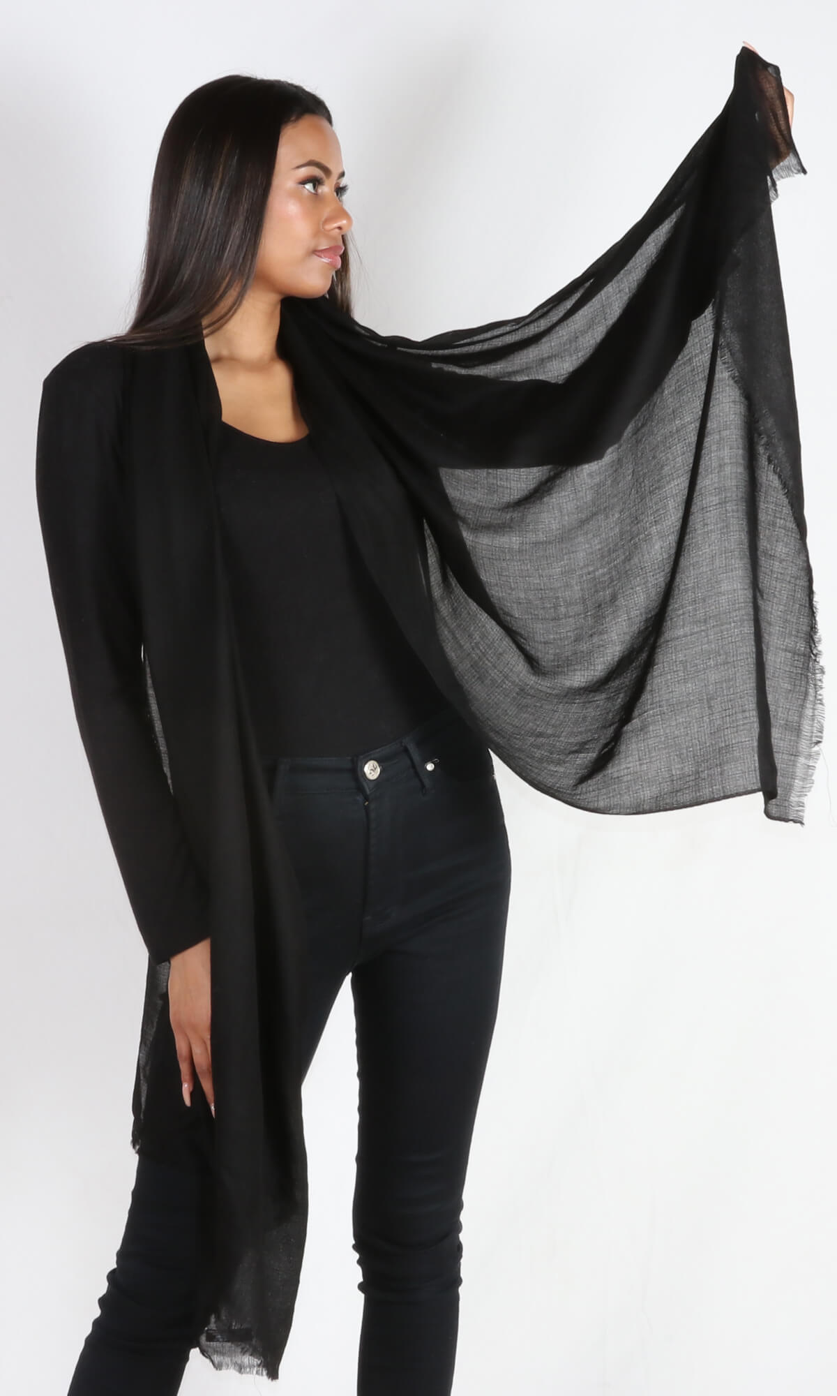 A 5ft 8 inches tall female model drapes a 100% pure handmade black cashmere shawl around her neck. She picks one edge of the shawls to show lightweight and transparent properties.