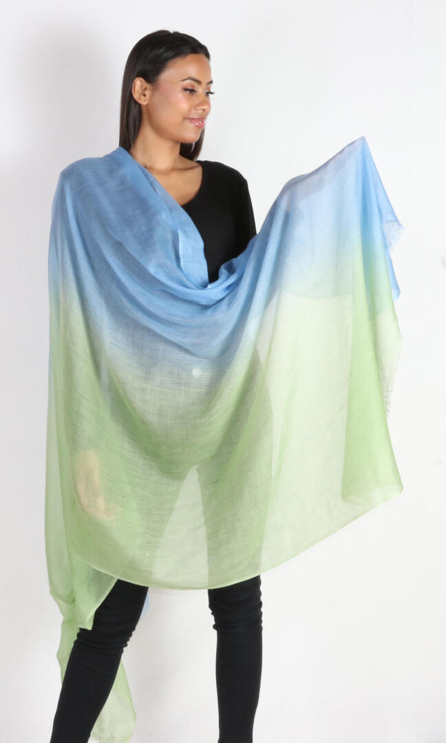 A beautiful model spreads the super light cashmere car shawl, an extra large wrap, to display its two colors, avocado and baby blue.