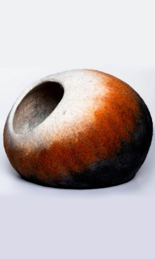 A handmade cat hideaway in the shape of an oval with a round entrance in black, deep orange, and white, with a left view.