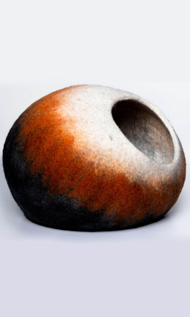 A handmade cat hideaway in the shape of an oval with a round entrance in black, deep orange, and white, with a right view.