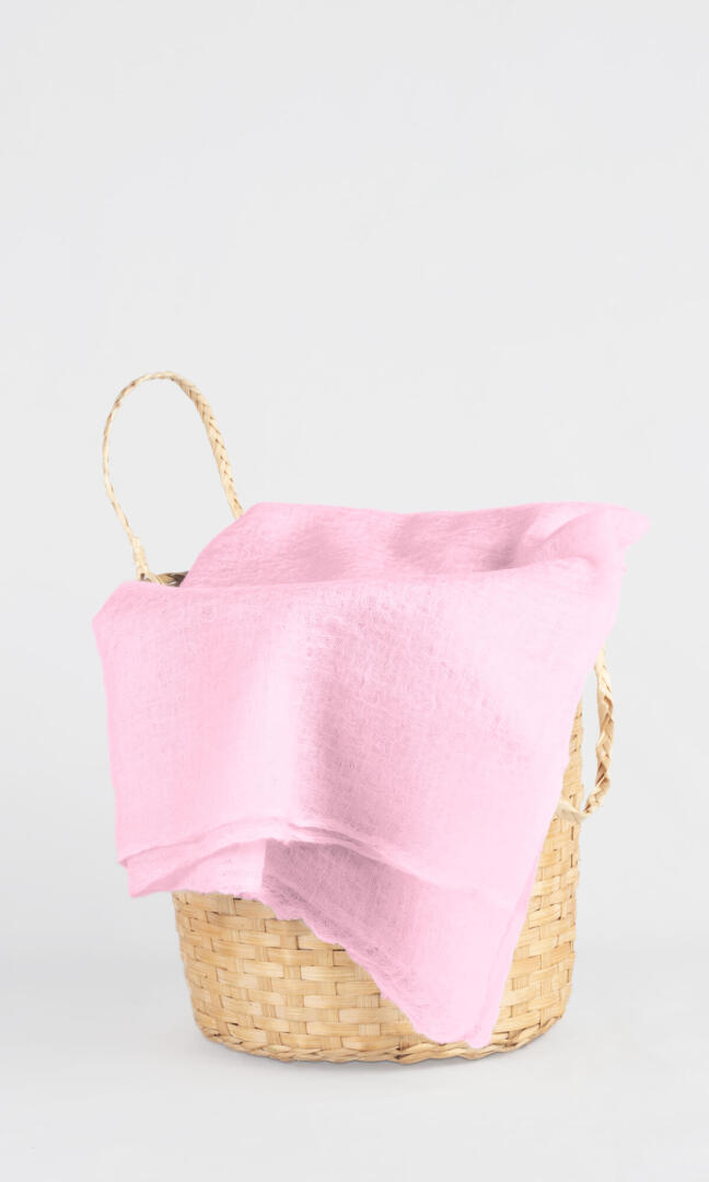 Full view of the premium handwoven 100% pure Baby Pink cashmere shawl draped over a bamboo basket.