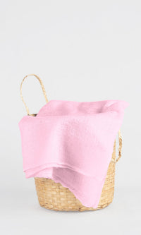 Full view of the premium handwoven 100% pure Baby Pink cashmere shawl draped over a bamboo basket.