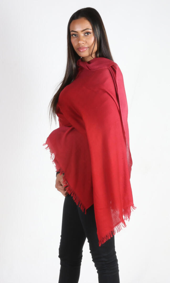 A female model displays a handmade two-tone red cashmere shawl wrapped around her body as a body wrap, a side view.