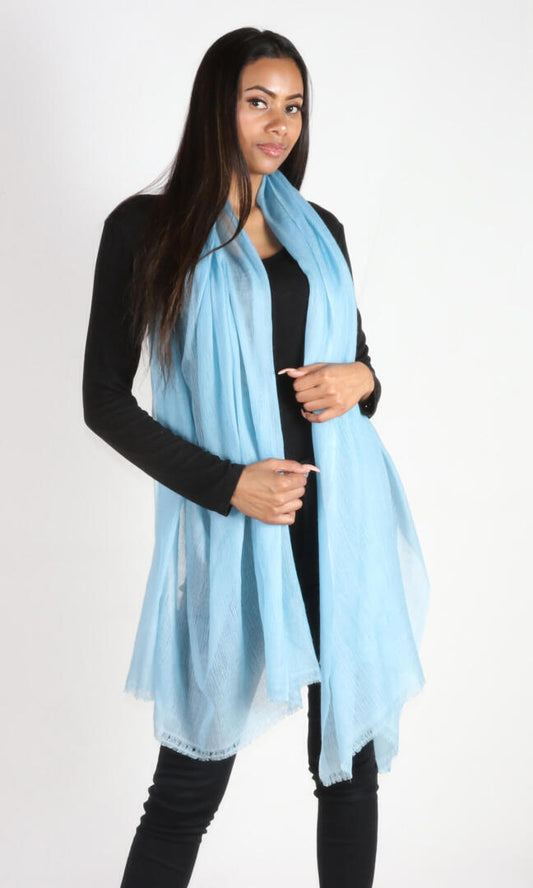 Woman wearing handmade aquamarine blue cashmere shawl draped around her neck. This luxurious shawl, perfect for March birthdays, is handcrafted and generously sized for comfortable coverage.