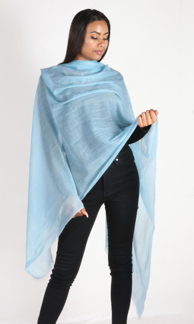 Woman wearing aquamarine blue cashmere shawl, front view. This luxurious shawl, perfect for March birthdays, is handcrafted and generously sized for comfortable coverage.