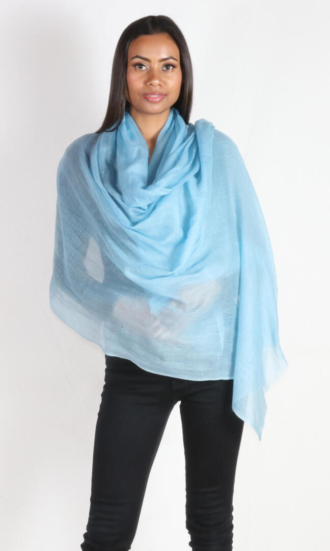 A beautiful female model displays a handmade cashmere shawl in aquamarine blue wrapped around her body to convey the message that the shawl is big enough to use as an evening wrap.